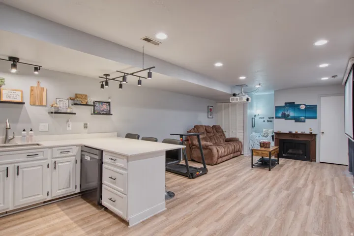 Finished lower level featuring wood-finish flooring, a built-in wet bar with white cabinetry and light-toned countertops, track lighting, recessed lighting, and a fireplace with a wood mantel