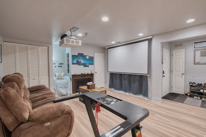Entertainment space featuring a ceiling-mounted projector, large pull-down screen, warm wood-finish flooring, recessed lighting, and a built-in fireplace