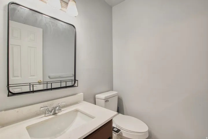 Bathroom featuring a rectangular mirror with integrated shelf, vanity with stone-look countertop, white undermount sink, and chrome faucet