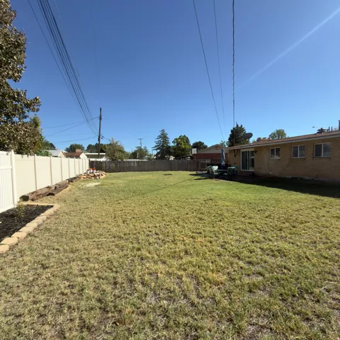 Expansive backyard featuring a manicured lawn, brick exterior, white vinyl fencing, and a patio with a sliding glass door