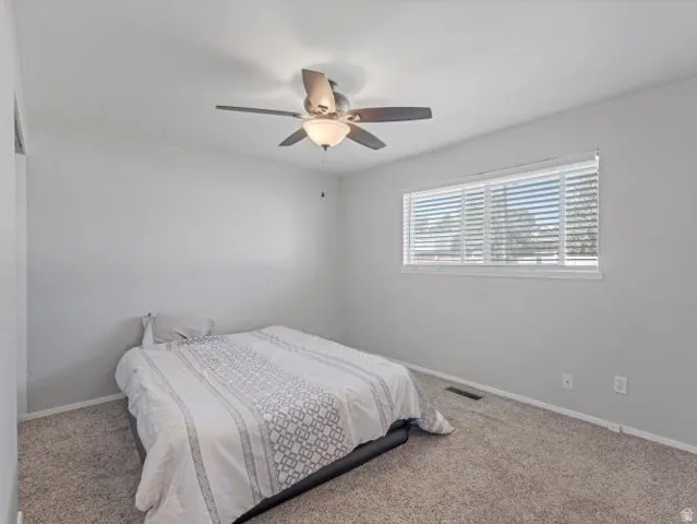Neutral wall color, ceiling fan with integrated lighting, window with horizontal blinds, and carpeted flooring