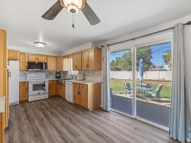 Kitchen featuring wood-finish flooring, wood cabinetry, white appliances, and a tile backsplash