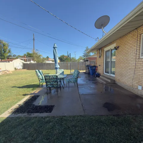 Expansive backyard featuring a concrete patio, a manicured lawn, and a light-colored brick exterior