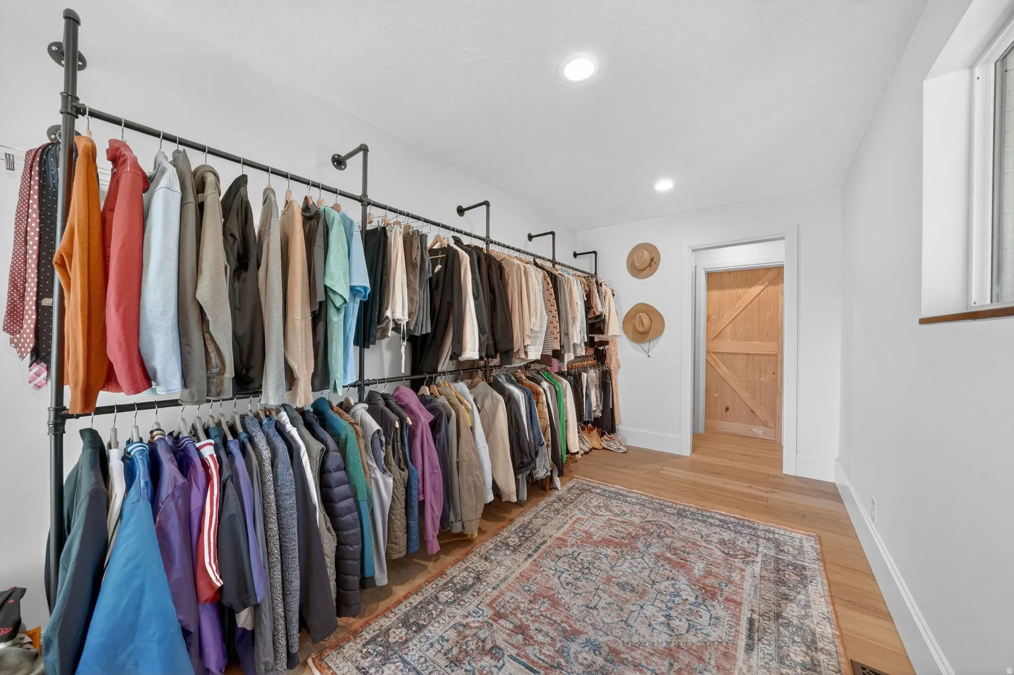 Built-in industrial-style clothing racks, light wood-finish flooring, recessed lighting, and a natural wood barn door