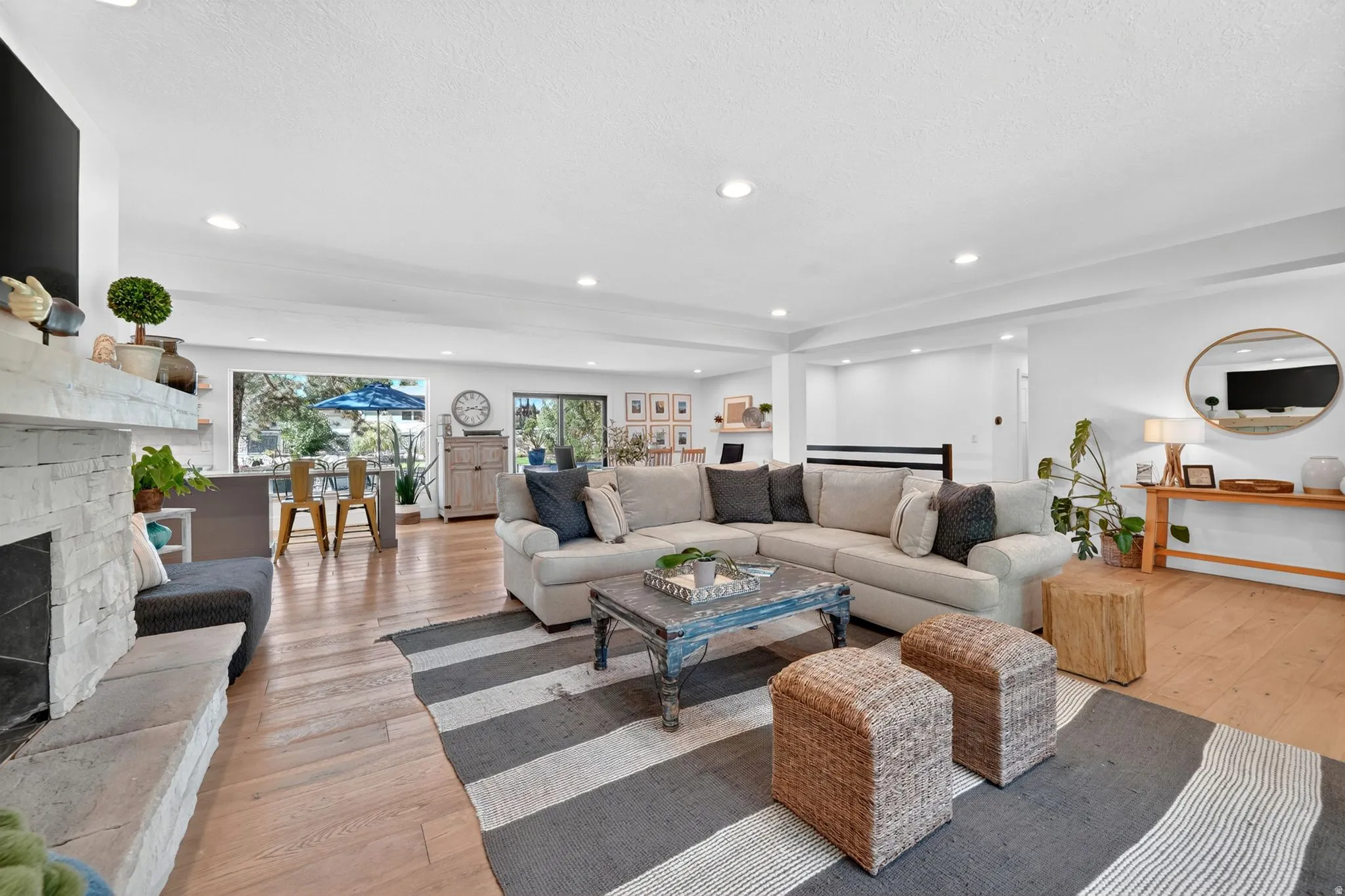 Spacious living area featuring wood-finish flooring, a stone fireplace with a hearth, recessed lighting, and expansive windows