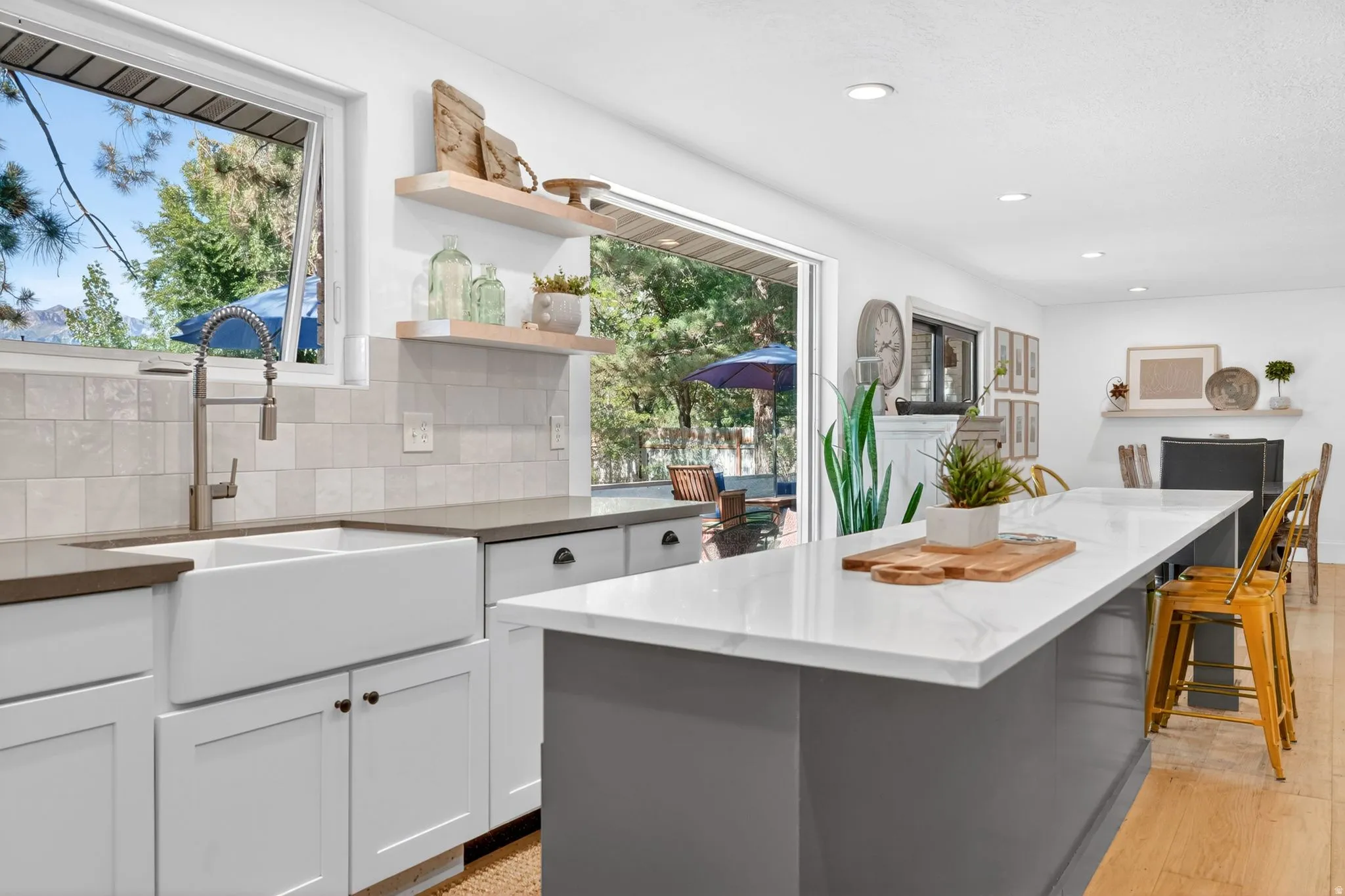 Bright kitchen featuring white shaker cabinetry, an apron-front sink, light-toned tiled backsplash, and a spacious island with a white countertop