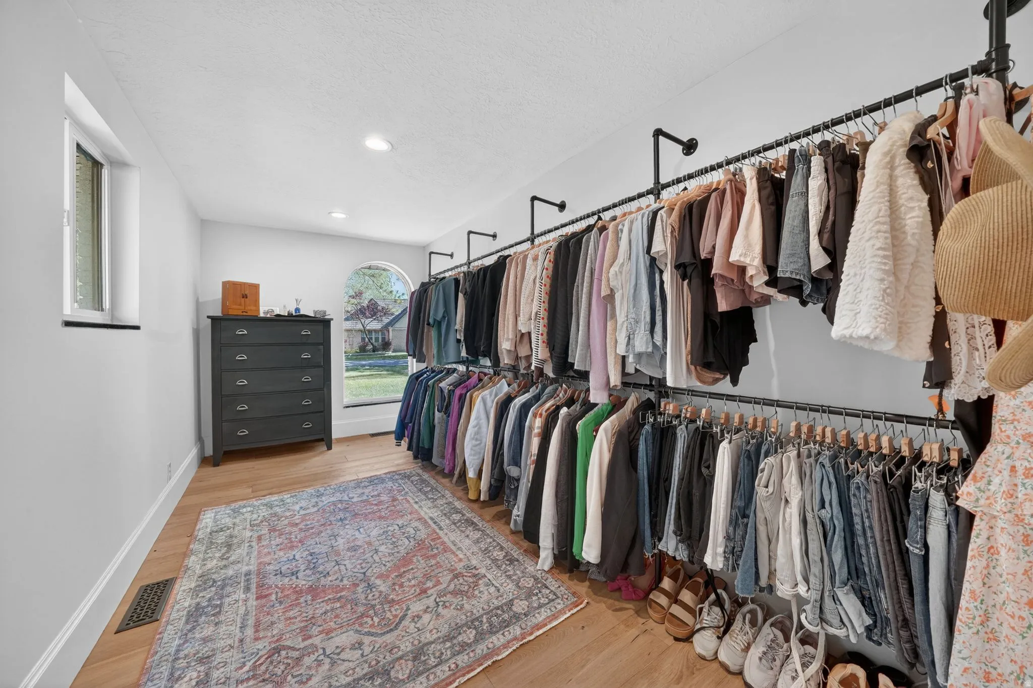 Expansive custom closet featuring extensive industrial-style clothing racks, wood-finish flooring, recessed lighting, a rectangular window, and an arched window providing natural light