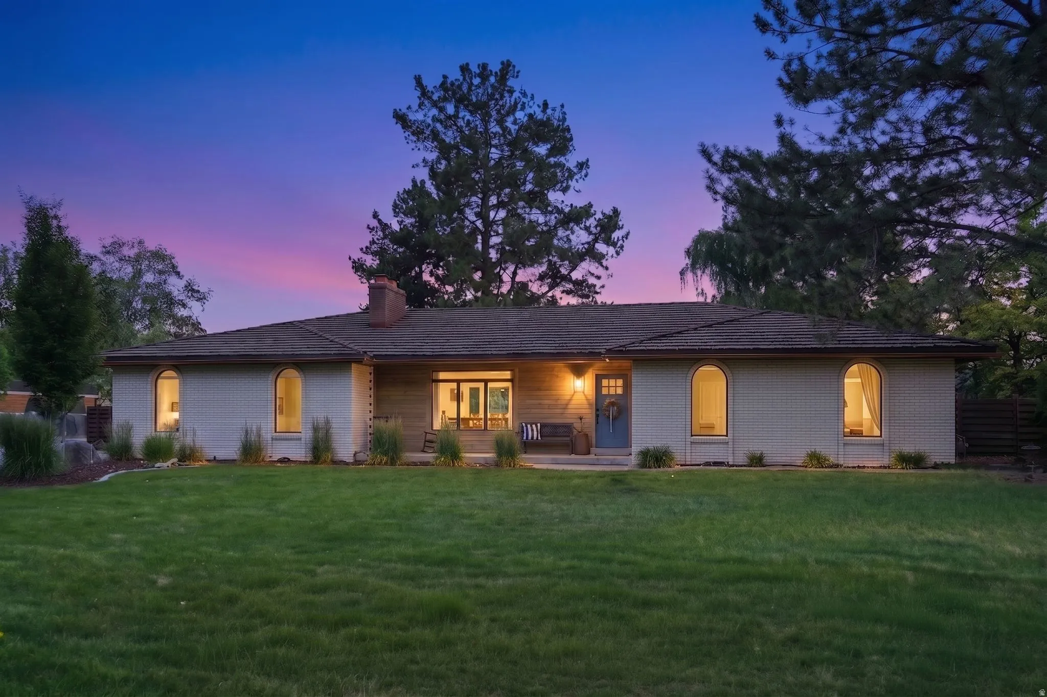 Ranch-style residence featuring a prominent front lawn, multiple arched windows, and a dark shingle roof