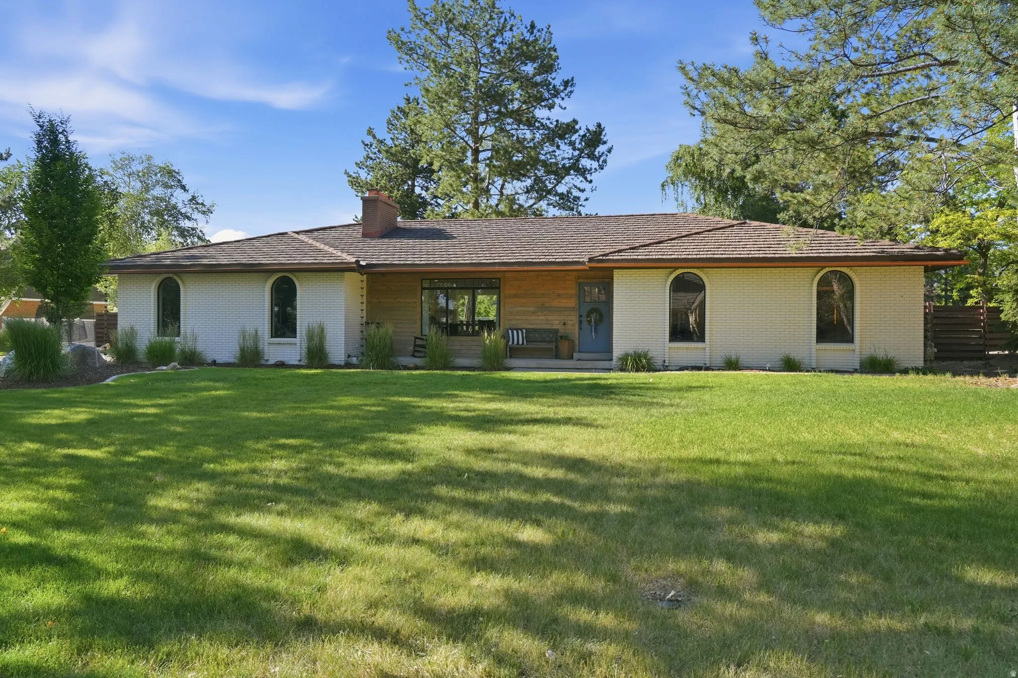 Ranch-style exterior with a brown shingle roof, white brick façade, and arched windows
