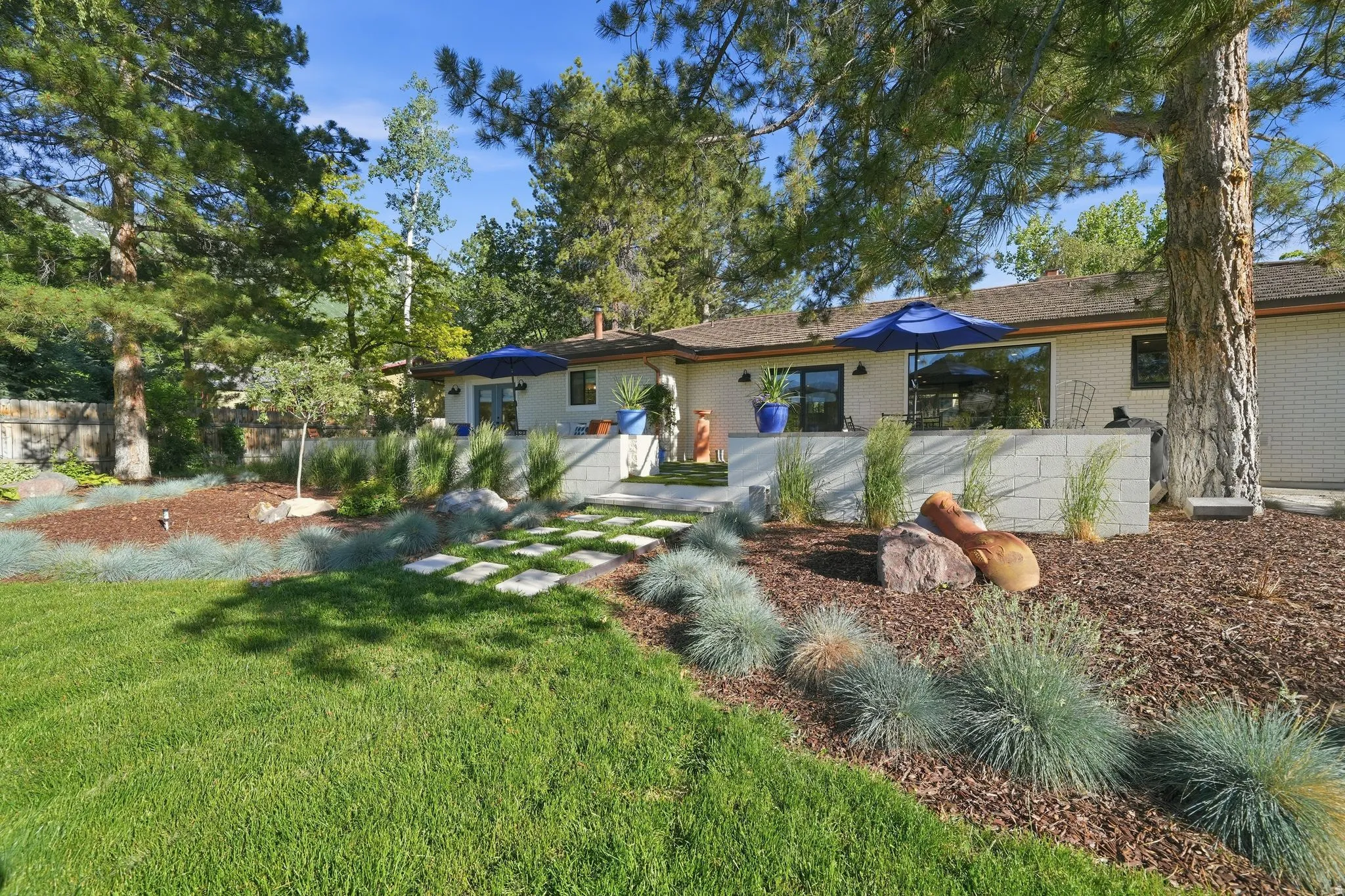 Extensive rear yard with a manicured lawn, established trees, and a contemporary patio featuring a tiled surface and white block retaining walls