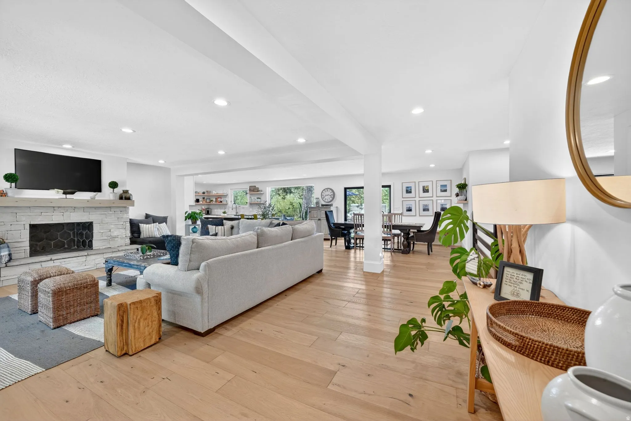 Spacious living area featuring light wood-finish flooring, a stacked stone fireplace, recessed lighting, and white walls