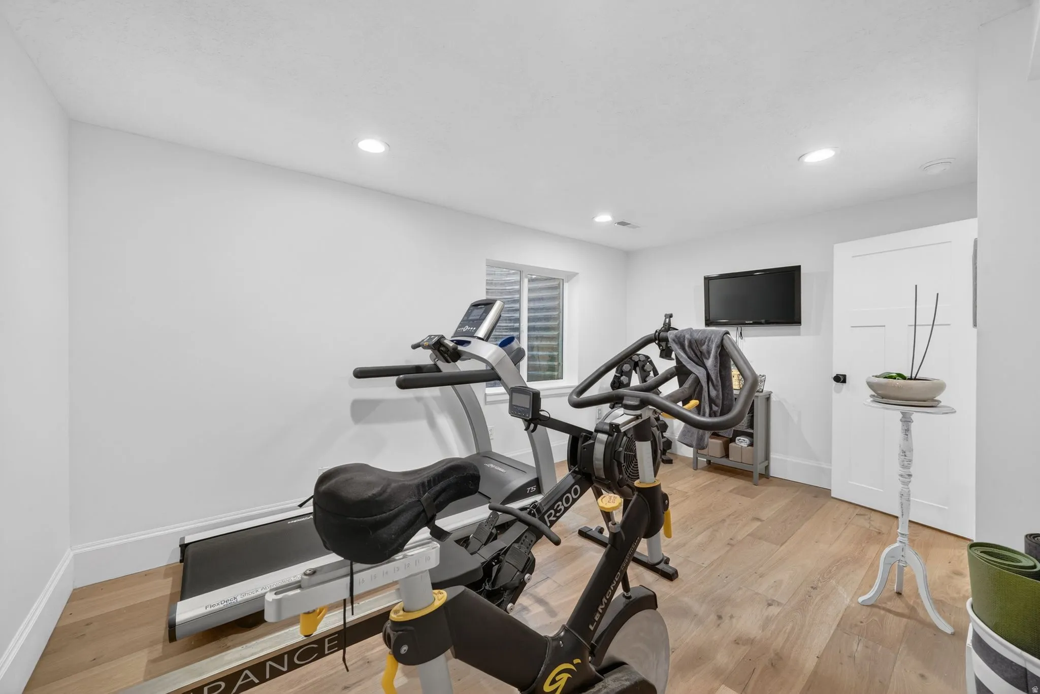 Spacious room with light wood-finish flooring, recessed lighting, and a white paneled door