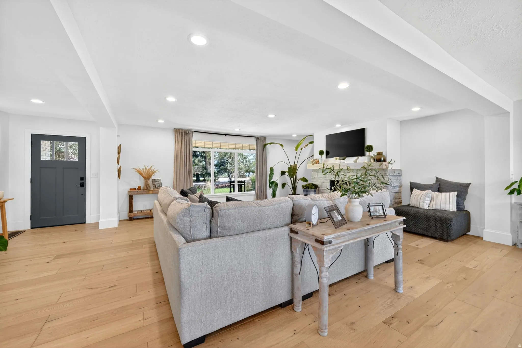 Spacious living area featuring light wood-finish flooring, recessed lighting, and a stone-clad fireplace with mantel