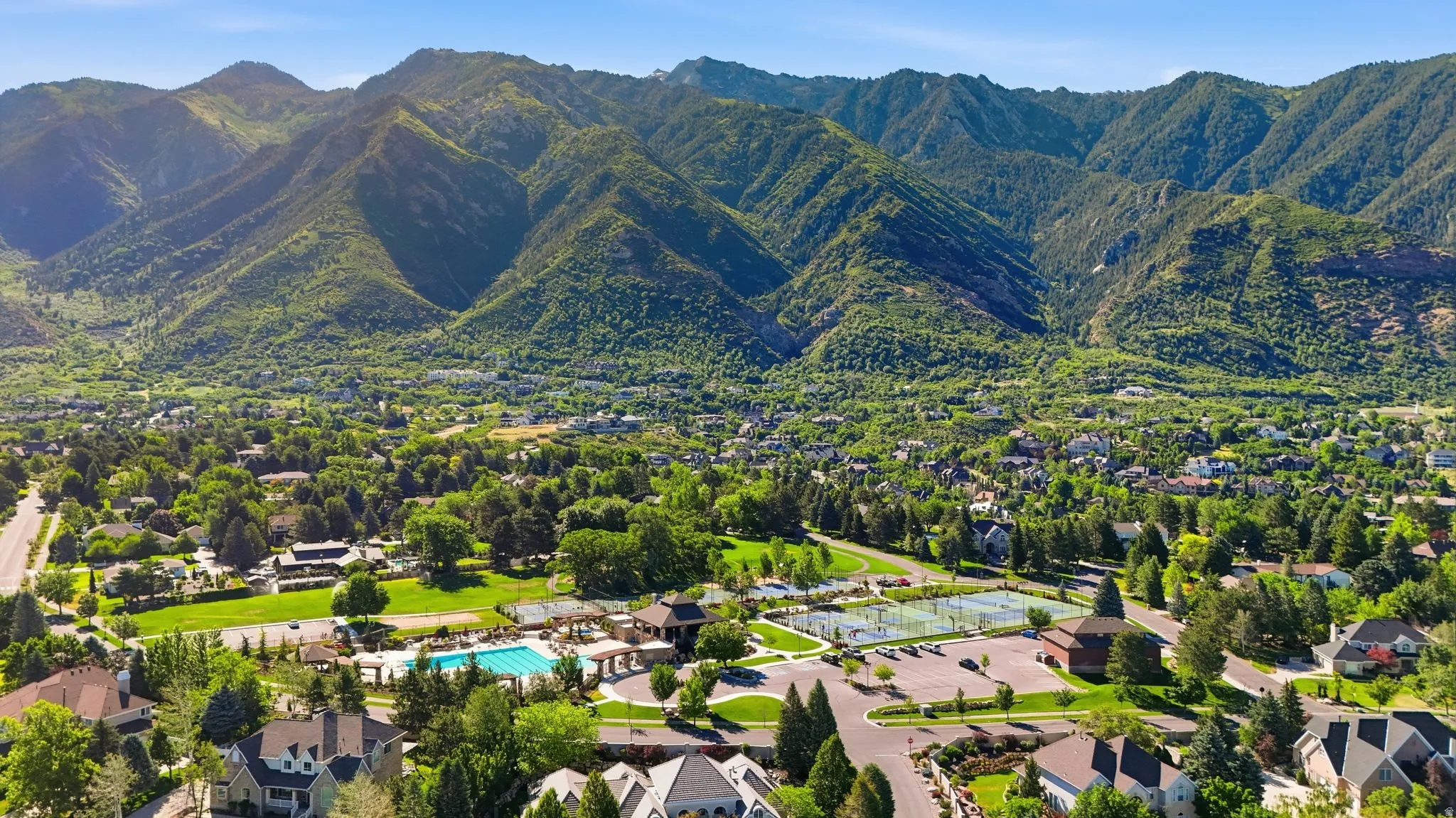 Expansive community featuring mature trees, a swimming pool, multiple tennis courts, and a mountainous backdrop