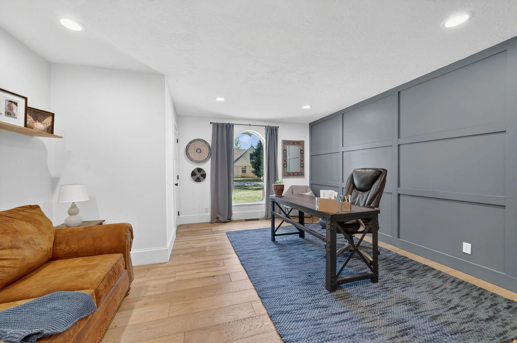 Accent wall with panel molding detail, recessed lighting, wood-finish flooring, and a large window with arched transom