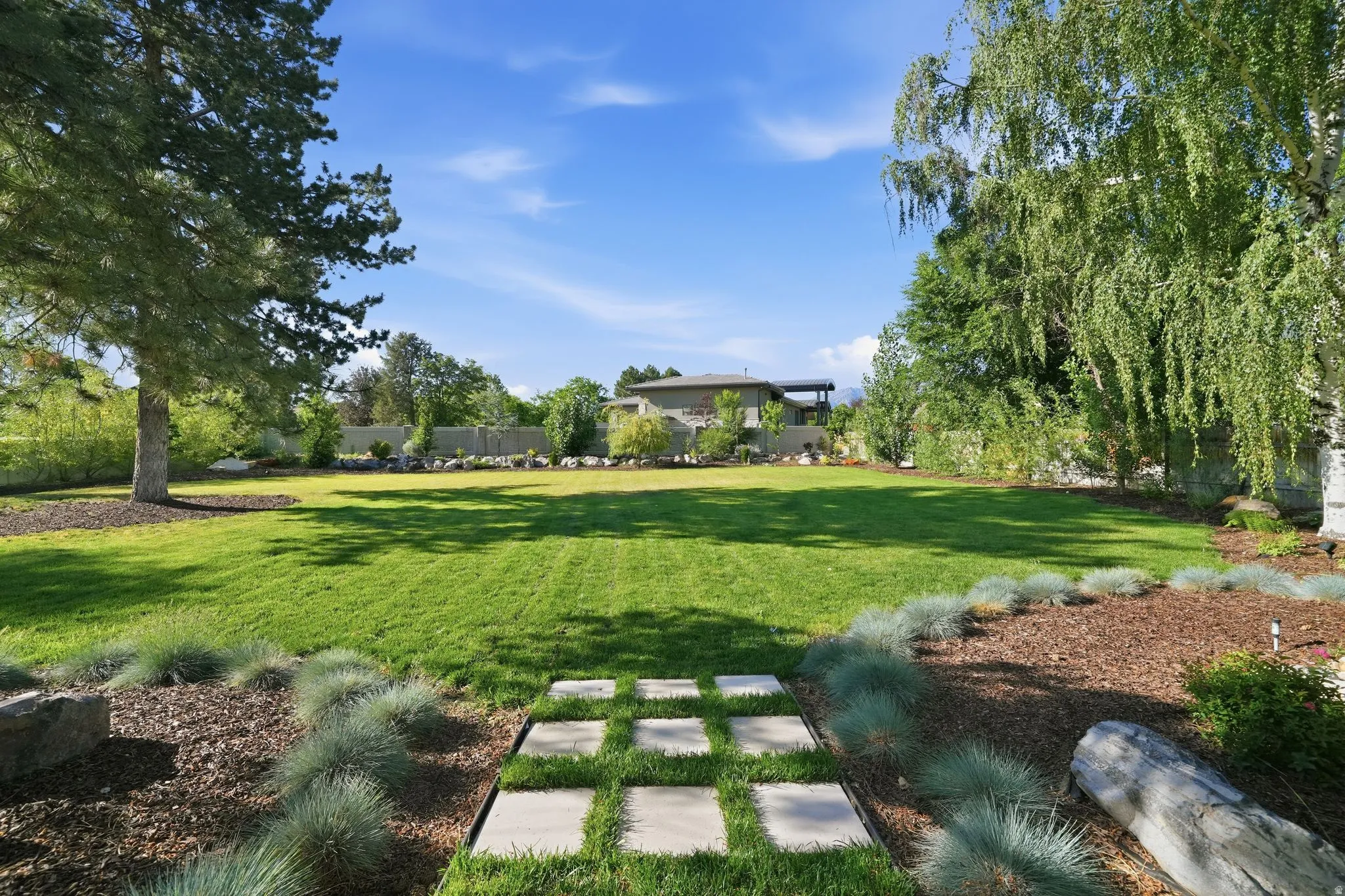 Expansive lawn featuring a stepping stone pathway, mature trees, and landscaped borders with ornamental grasses and woodchip ground cover