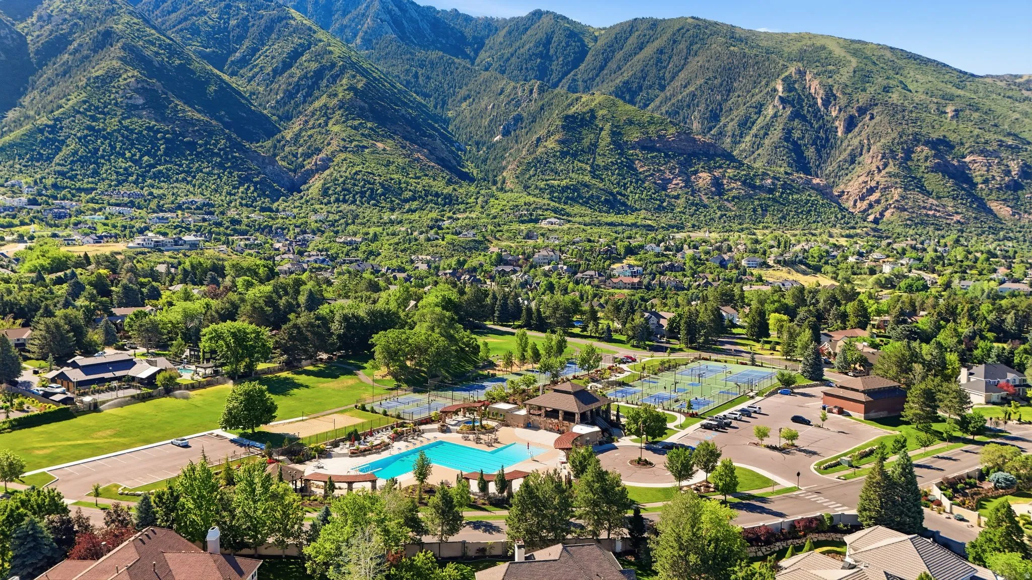 Expansive community amenity area featuring a large swimming pool, multiple tennis courts, and a clubhouse building