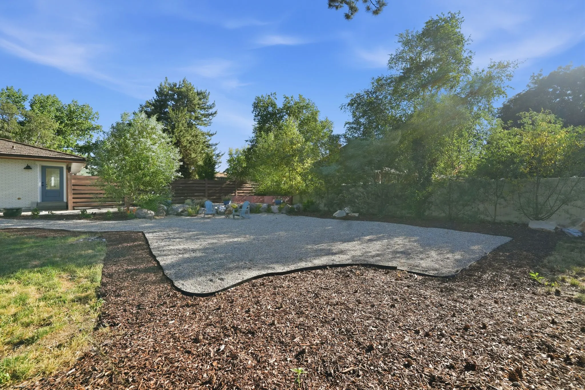 Expansive outdoor space featuring a large gravel patio area, surrounded by decorative wood mulch, and a manicured lawn strip
