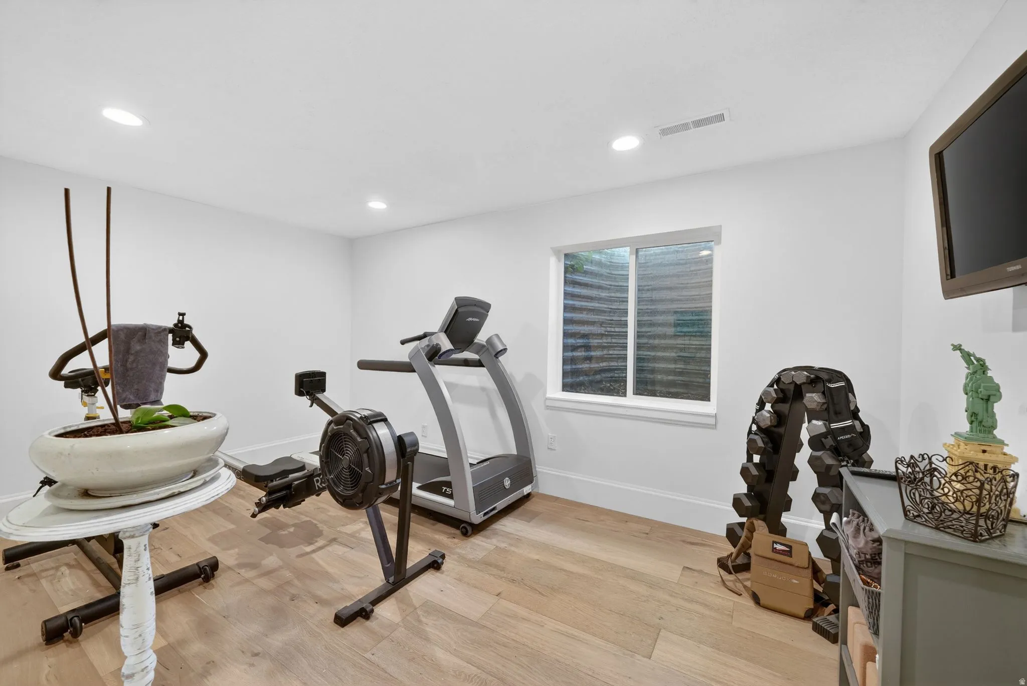 Bright room with light wood-finish flooring, recessed lighting, and a window providing natural illumination