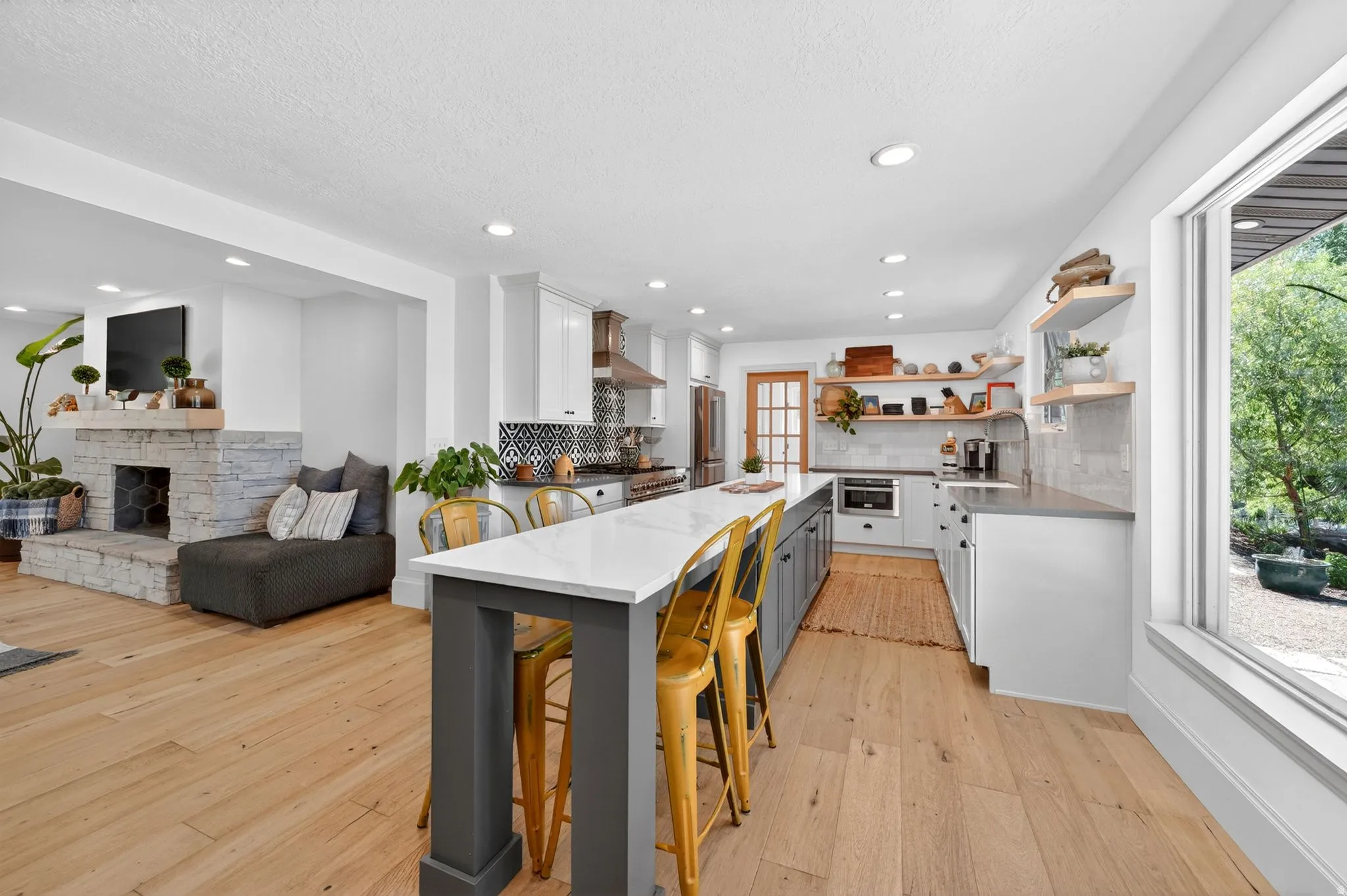 Open-concept kitchen featuring a large central island with seating, extensive wood-finish flooring, a stone fireplace, recessed lighting, and a large picture window