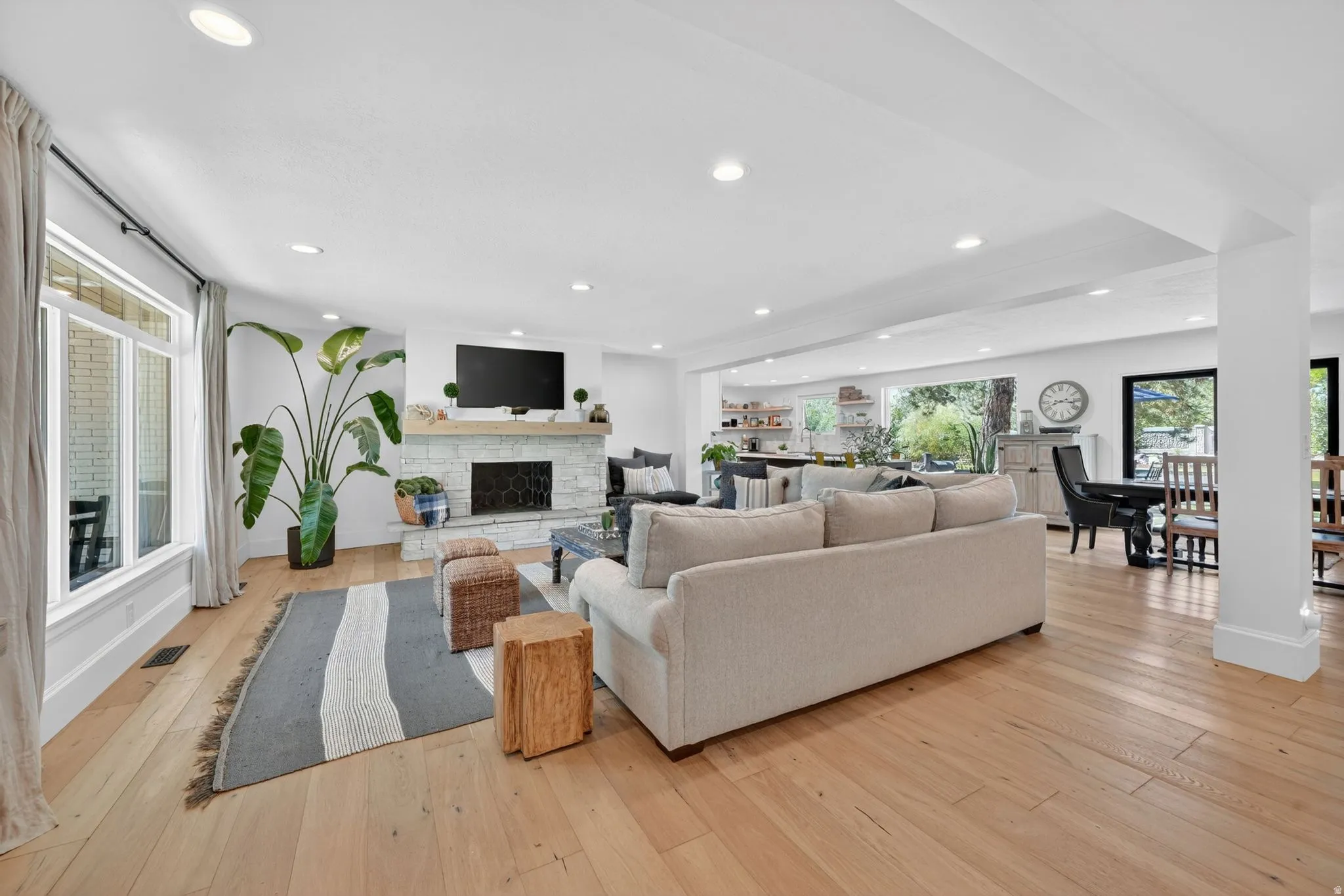 Expansive living area featuring light wood-finish flooring, recessed lighting, and a white brick fireplace with a wood mantel