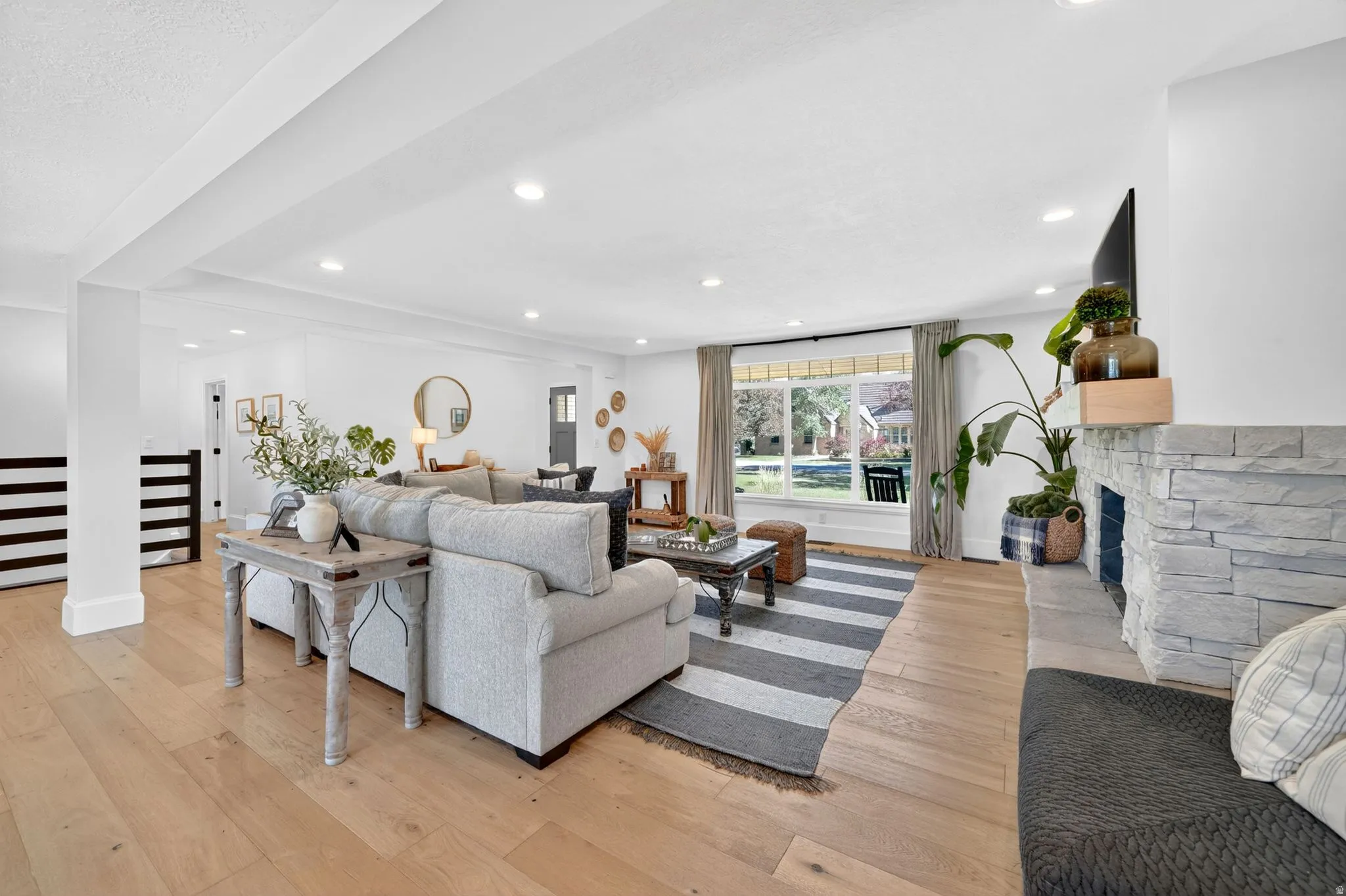 Spacious living area featuring light wood-finish flooring, a stacked stone fireplace with a wood mantle, and recessed lighting