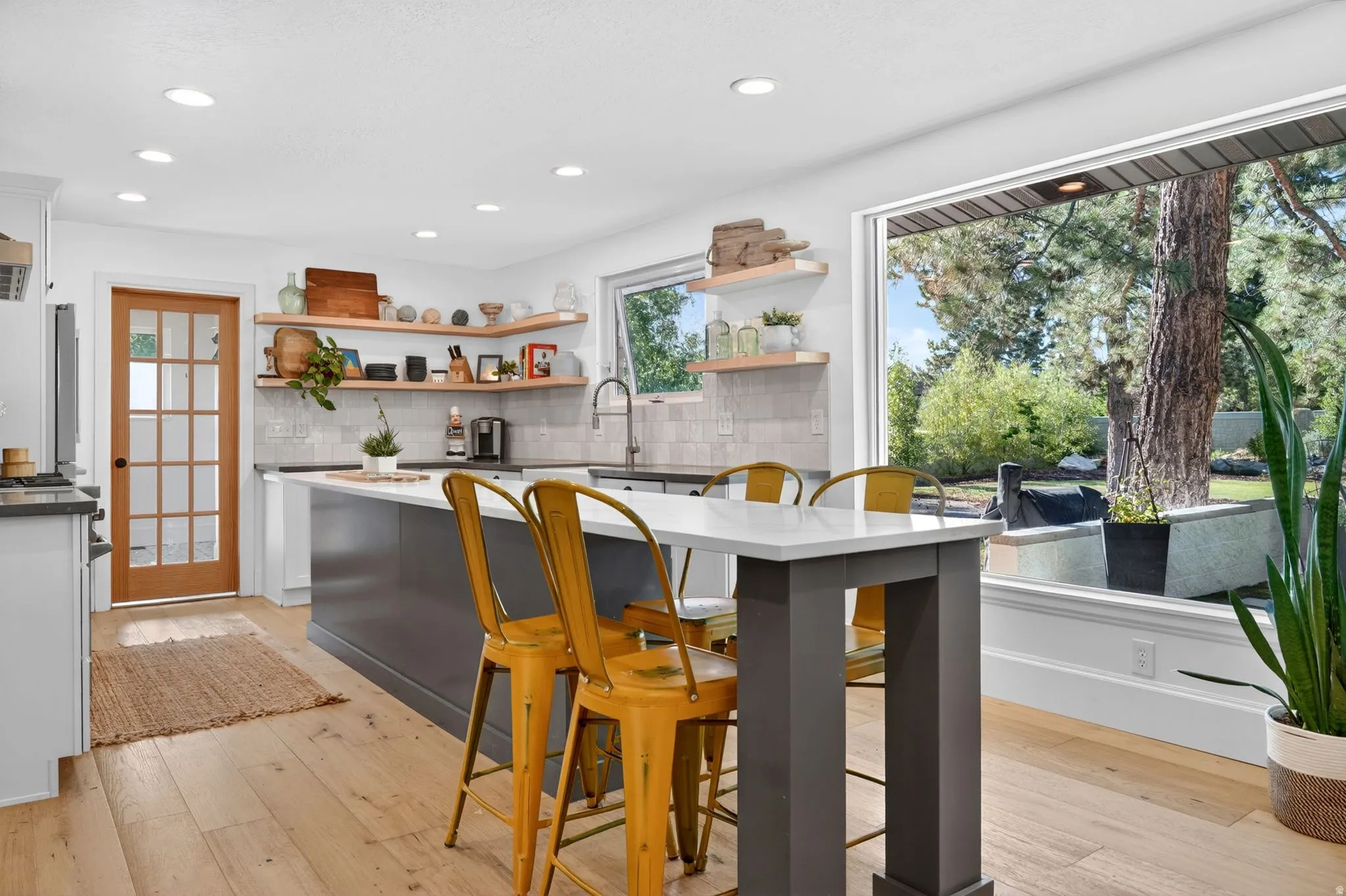 Open-concept kitchen featuring an island with seating, light wood-finish flooring, recessed lighting, white perimeter cabinetry, and a large picture window