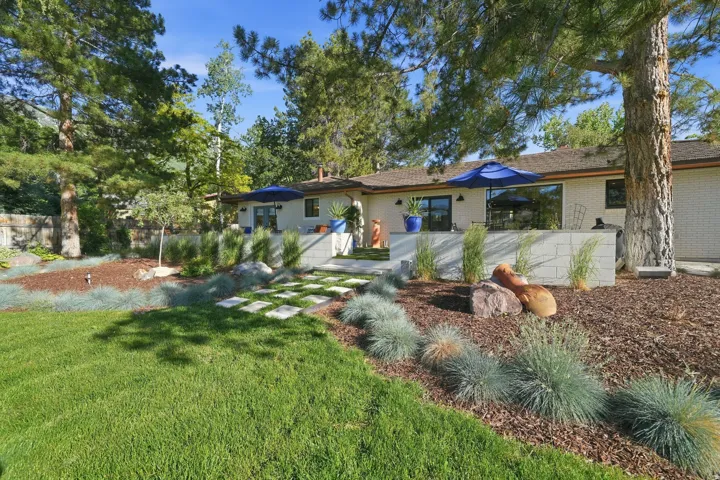 Extensive rear yard with a manicured lawn, established trees, and a contemporary patio featuring a tiled surface and white block retaining walls