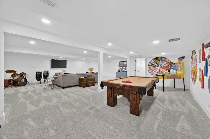 Spacious recreation room featuring light gray patterned carpeting, recessed lighting, and white walls