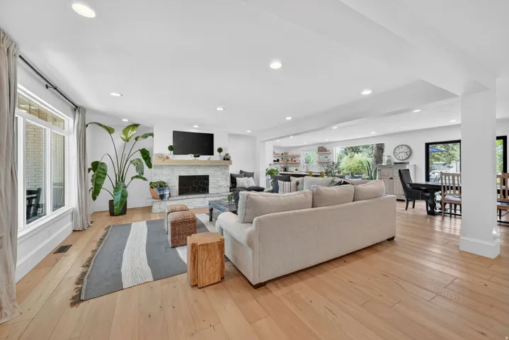 Expansive living area featuring light wood-finish flooring, recessed lighting, and a white brick fireplace with a wood mantel