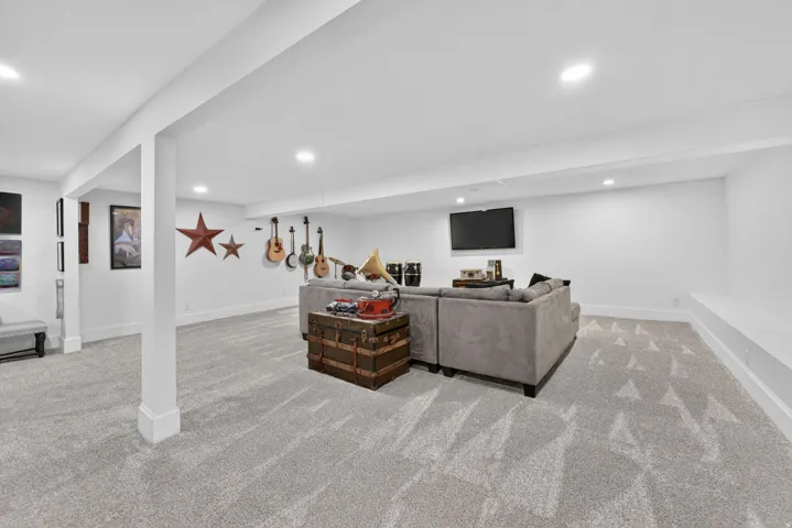 Spacious finished basement featuring recessed lighting, light-toned patterned carpeting, crisp white walls, and a built-in wall bench