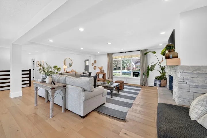 Spacious living area featuring light wood-finish flooring, a stacked stone fireplace with a wood mantle, and recessed lighting