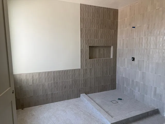Primary Suite walk-in shower with vertical tile work, integrated shower niche, floor-to-ceiling tiling, and a tiled shower pan