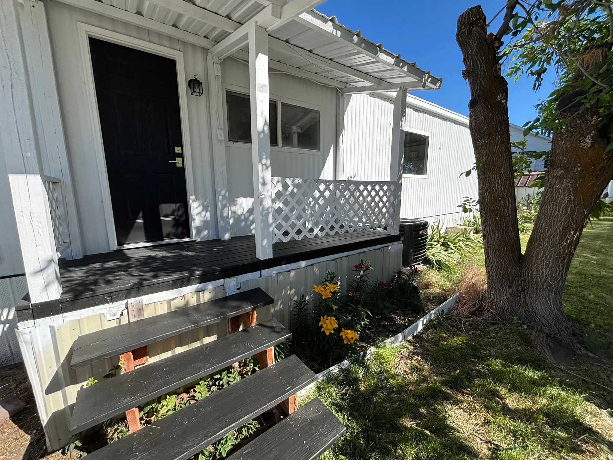 Front entrance featuring a black paneled door with gold-tone hardware, covered porch with white lattice railing, and multi-tiered steps