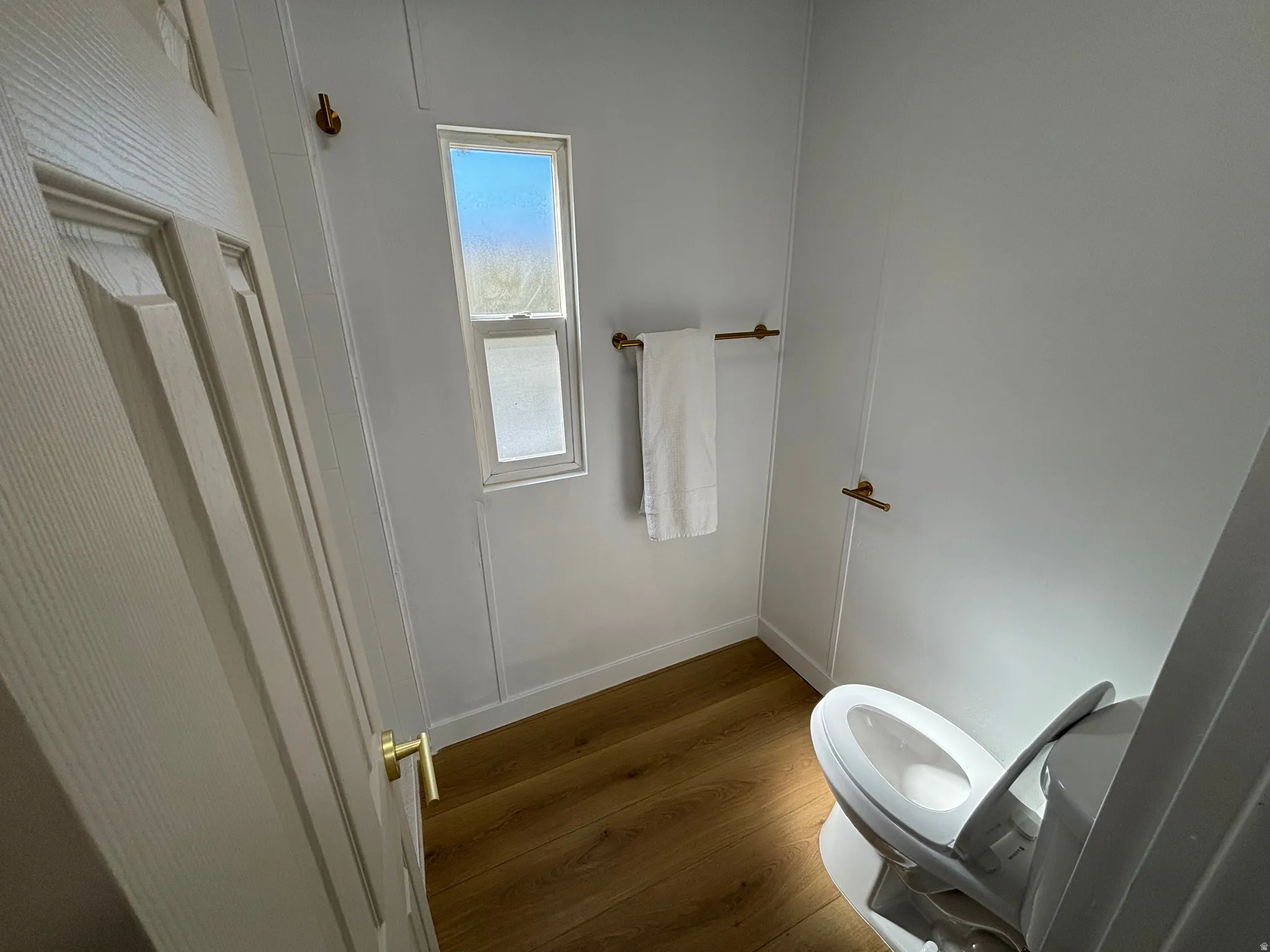 Bathroom featuring wood-finish flooring, a contemporary toilet, and a window providing natural illumination