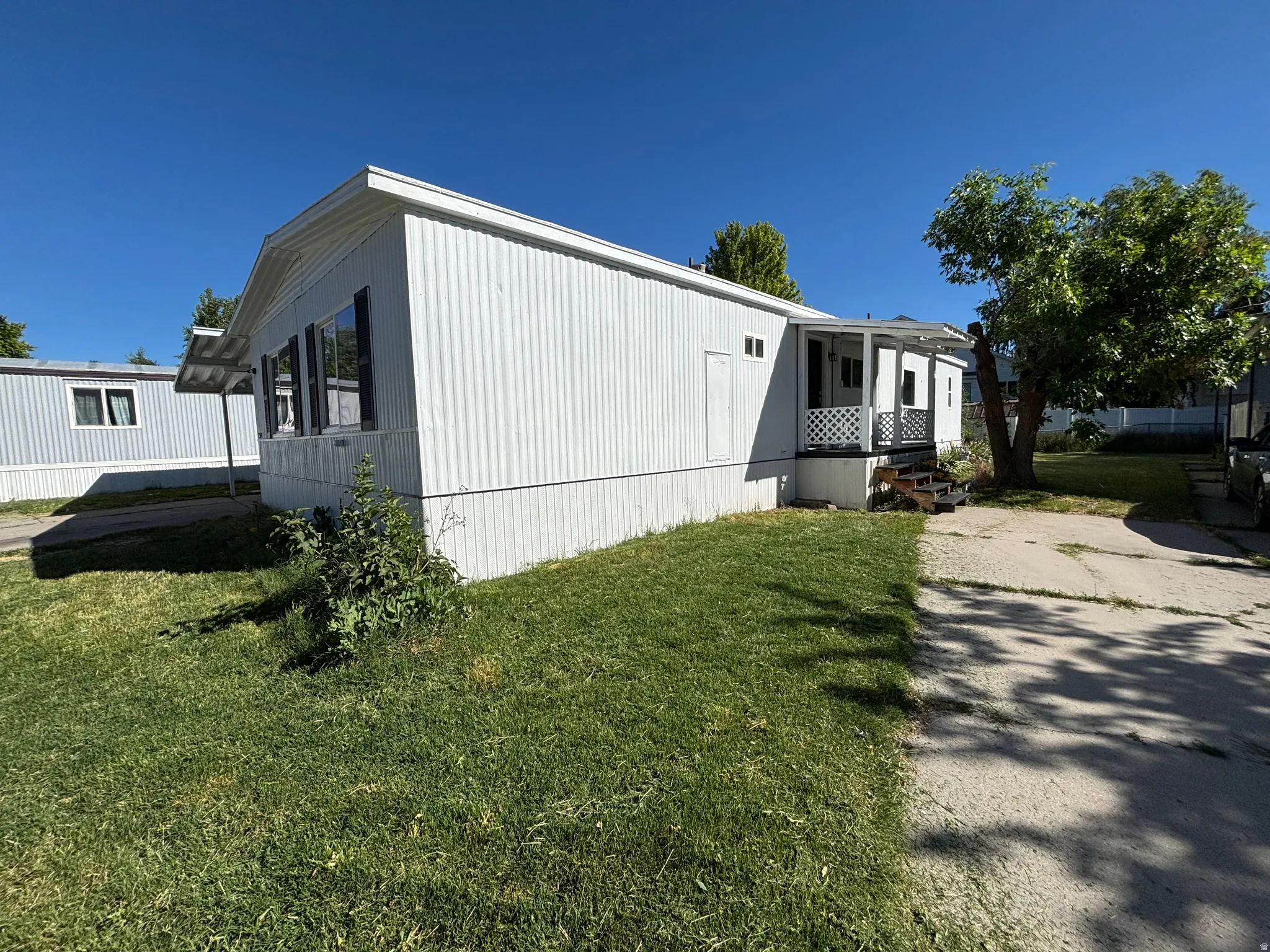 White manufactured home featuring horizontal siding and a covered front porch with lattice detailing