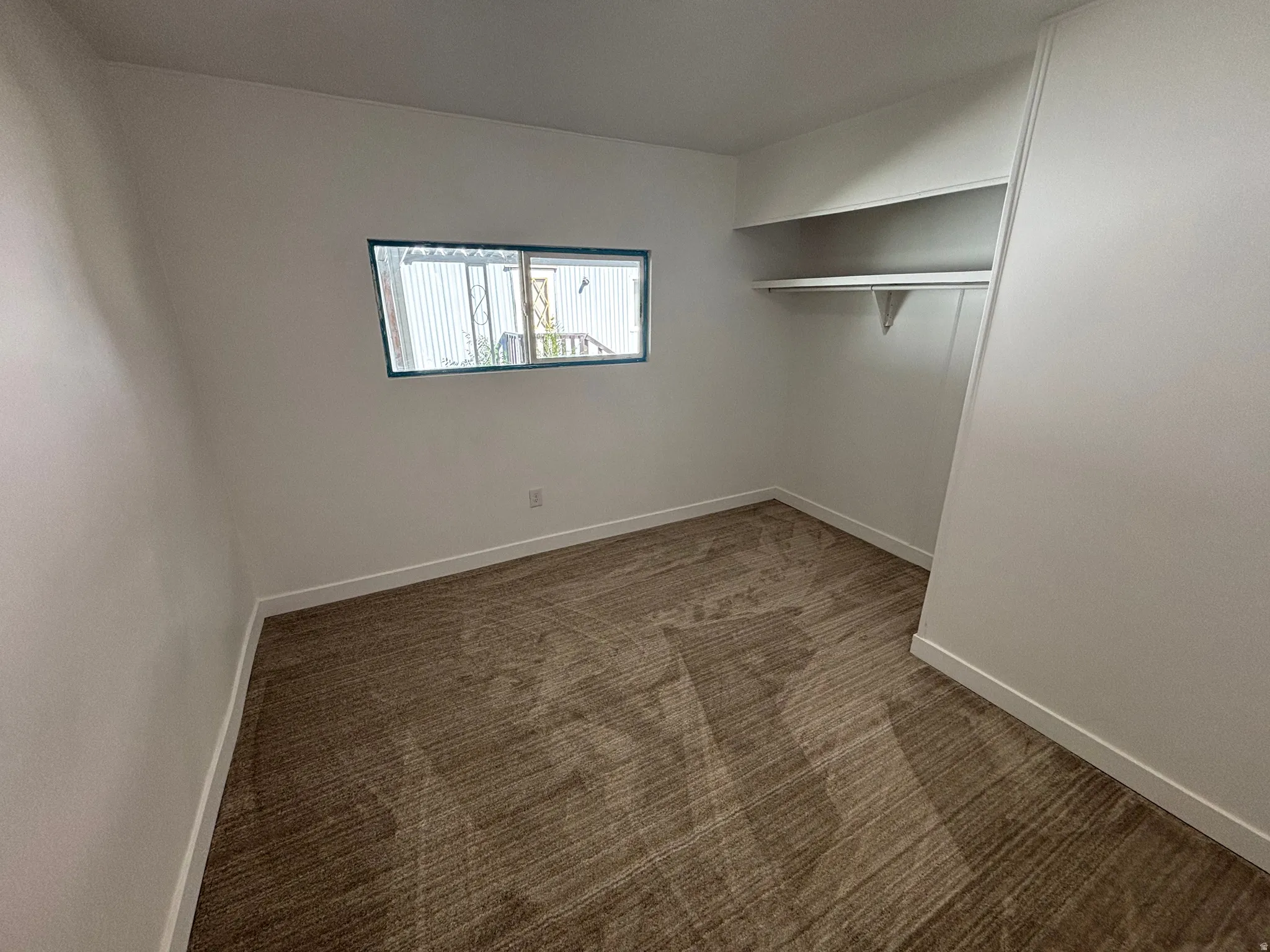 Carpeted room with white walls, baseboards, a horizontal window, and built-in closet shelving