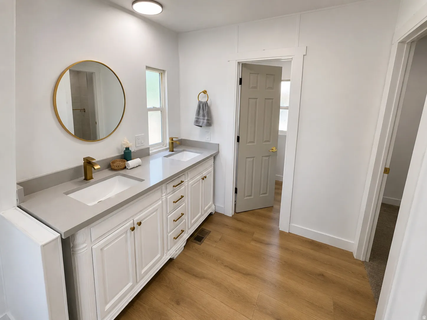Double vanity featuring white cabinetry, integrated sinks, brass-finish fixtures, and a light gray countertop