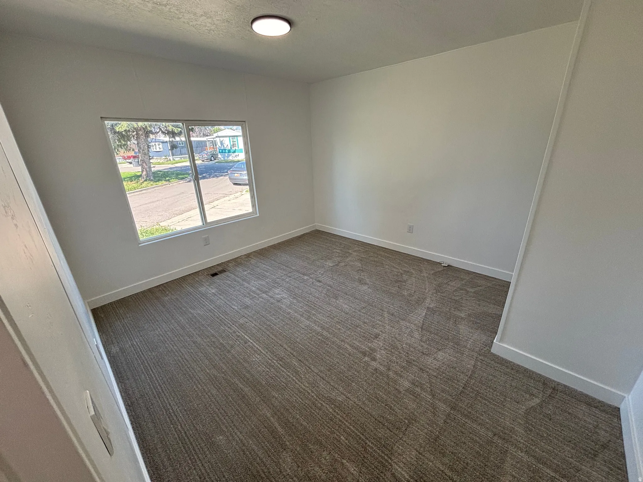 Spacious room featuring neutral carpeting, white walls, a large window, and a flush-mount ceiling light