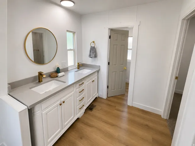 Double vanity featuring white cabinetry, integrated sinks, brass-finish fixtures, and a light gray countertop