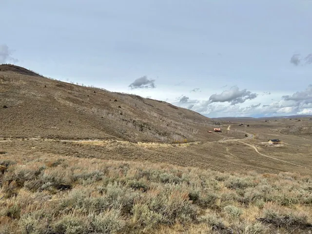 Expansive open terrain with natural vegetation and distant structures