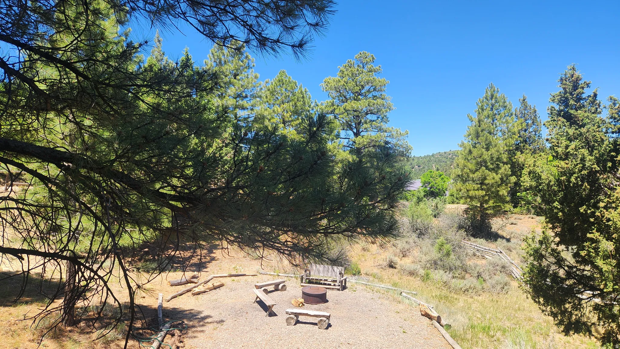 Outdoor gathering area featuring a central fire pit, surrounding log benches, and a gravel surface