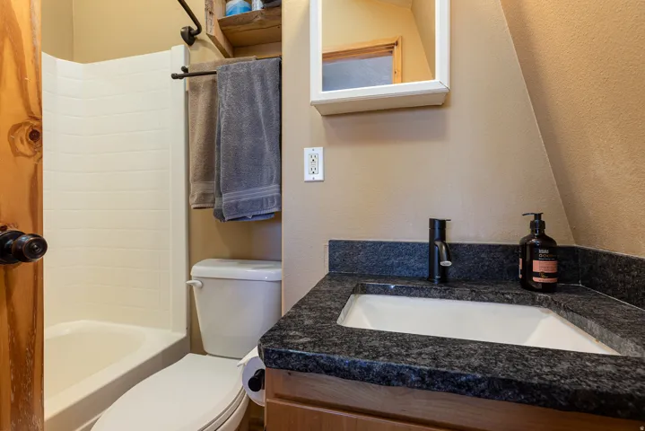Ensuite Bathroom featuring a white shower-tub combination, a white toilet, a vanity with a dark speckled countertop, a white rectangular undermount sink, and a black single-handle faucet