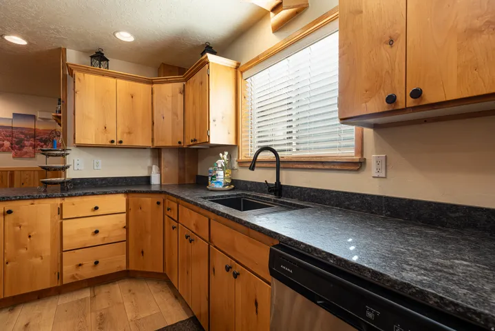 Kitchen featuring wood-finish cabinetry with black hardware, dark countertops, a black sink with a matte black faucet, and wood-finish flooring