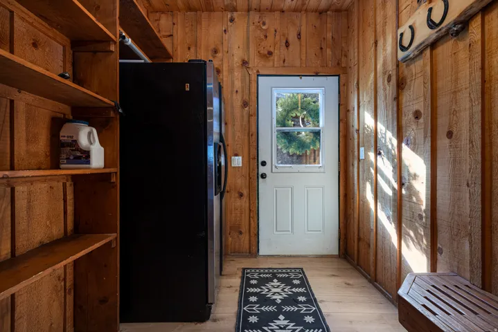 Utility room featuring wood-finish wall and ceiling paneling, a full-size refrigerator, built-in shelving, a white door with a window pane, and light wood-finish flooring