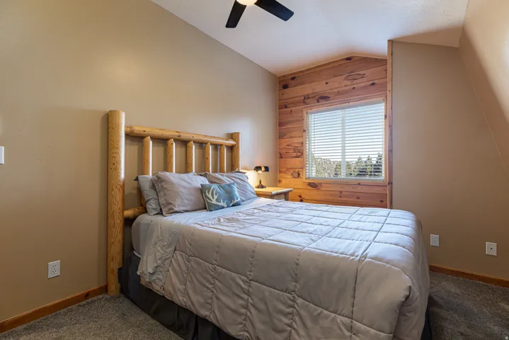 Bedroom featuring a wood-paneled accent wall, a window with horizontal blinds, textured beige walls, and sloped ceilings