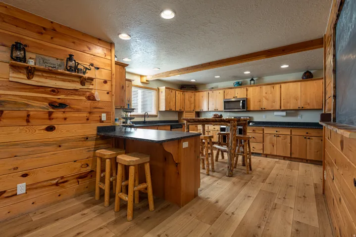 Kitchen featuring extensive wood-finish wall paneling, perimeter cabinetry with dark countertops, wood-finish flooring, a built-in microwave, and recessed lighting