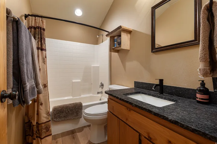Bathroom featuring a white subway tile shower surround, a built-in bathtub, a wood-finish vanity with an integrated sink, a dark speckled countertop, and wood-finish flooring