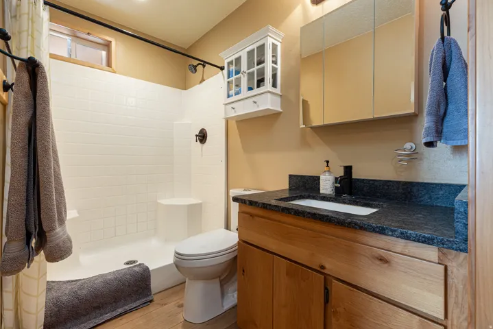 Bathroom featuring a shower with white subway tile surround and integrated bench, a wood-finish vanity with a dark speckled countertop, an undermount sink, and a black single-handle faucet