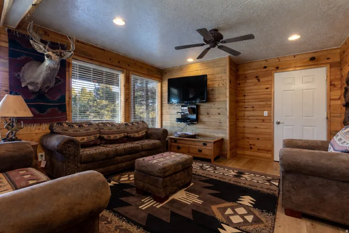 Living area featuring natural wood-paneled walls, wood-finish flooring, recessed lighting, and a ceiling fan with integrated lighting